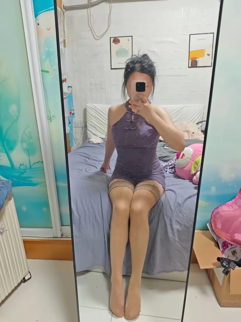 镜子正面自拍，全身坐在床沿，紫色蕾丝包臀裙＋肤色吊带丝袜，卧室内有抱枕与装饰画。