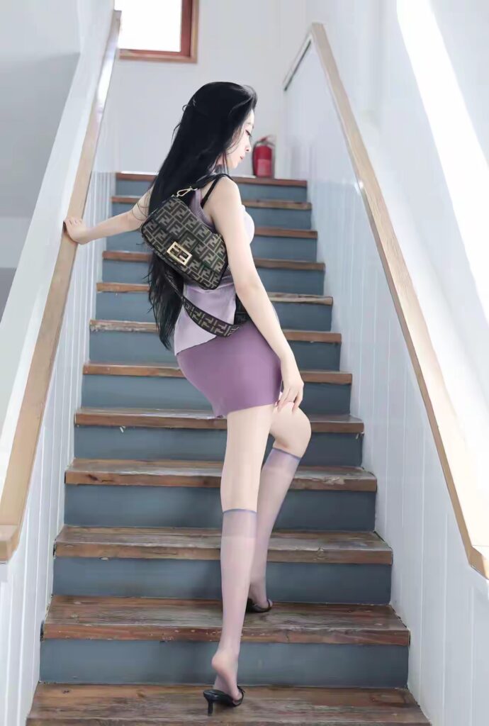 同一楼梯间，女生背单肩老花腋下包，侧身上楼；紫色包臀裙＋淡紫中筒丝袜与黑色高跟拖鞋。