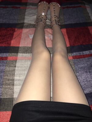 格纹床单上，穿肤感丝袜的双腿并拢伸直，脚上为红色尖头铆钉细带高跟鞋，画面从膝部向下拍摄。