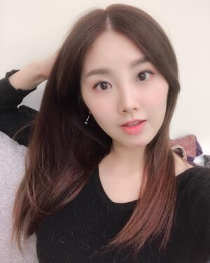 女生在室内微笑自拍，穿黑色上衣，长发披肩，灯光柔和。