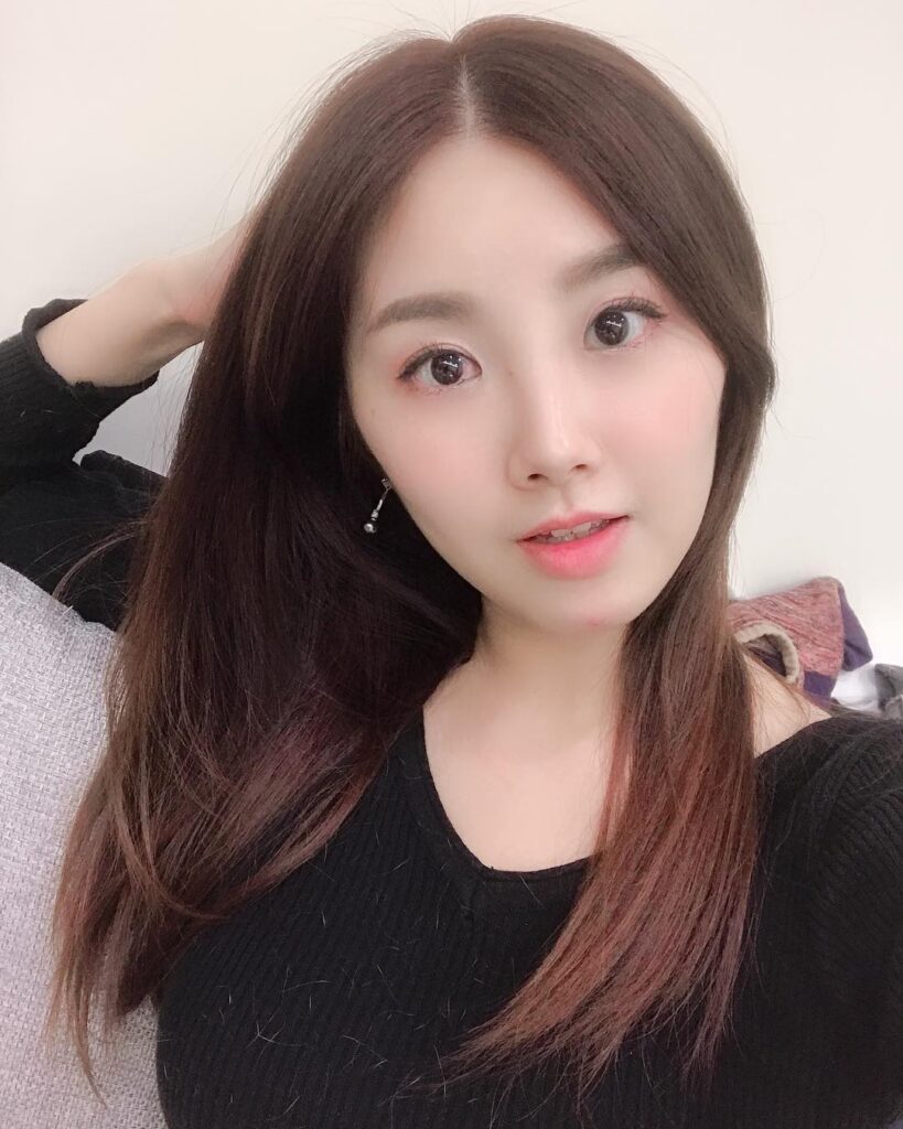女生在室内微笑自拍，穿黑色上衣，长发披肩，灯光柔和。