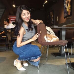 咖啡馆里，女生蹲在椅旁对镜头微笑，椅上蜷着一只橘白色小兔，室内昏暖，画面轻松自在。