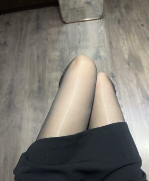 室内木地板上方的俯拍视角，黑色短裙与薄丝袜包裹的双腿并拢坐姿，暖光干净、画面简洁。