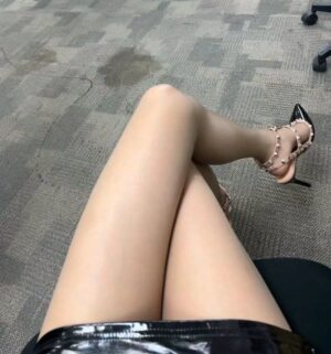 办公室地毯上方的俯拍视角，黑亮短裙与肤色丝袜，双腿自然交叉，铆钉高跟鞋点缀，画面干净克制。