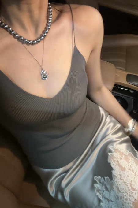 车内座椅上的女孩，灰色针织吊带配银灰缎面裙与珍珠项链。