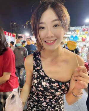 女生在夜市摊位前惊喜表情，手持小吃串，身后招牌与人群清晰可见。